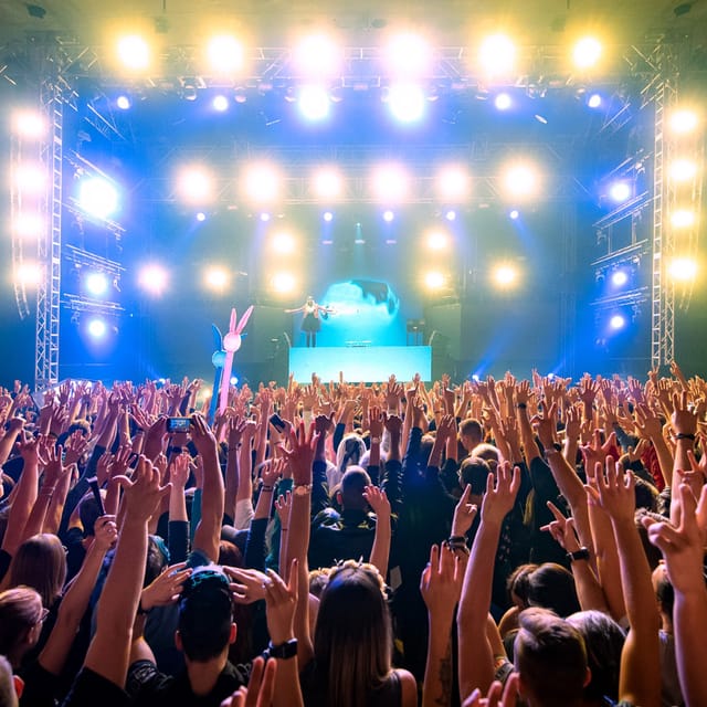A packed indoor crowd raising their hands toward CANDICE on a brightly lit festival stage