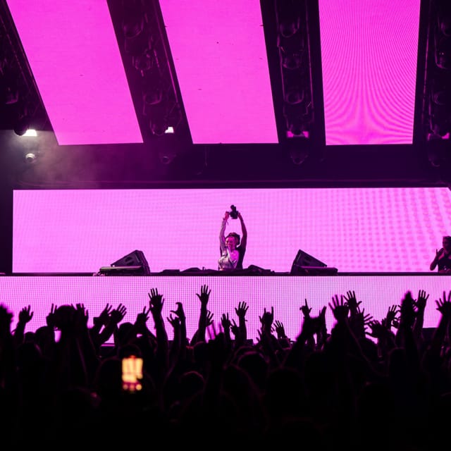CANDICE lifting her headphones above the DJ booth against bright pink stage screens
