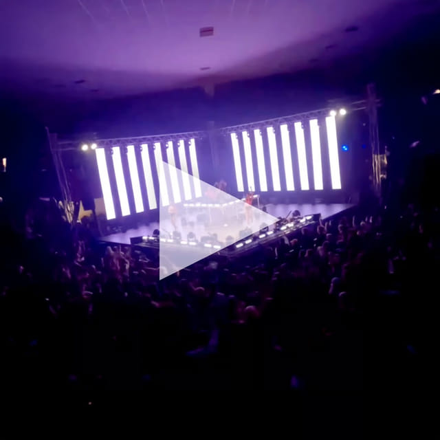 Wide audience view of a DJ stage framed by bright vertical LED panels